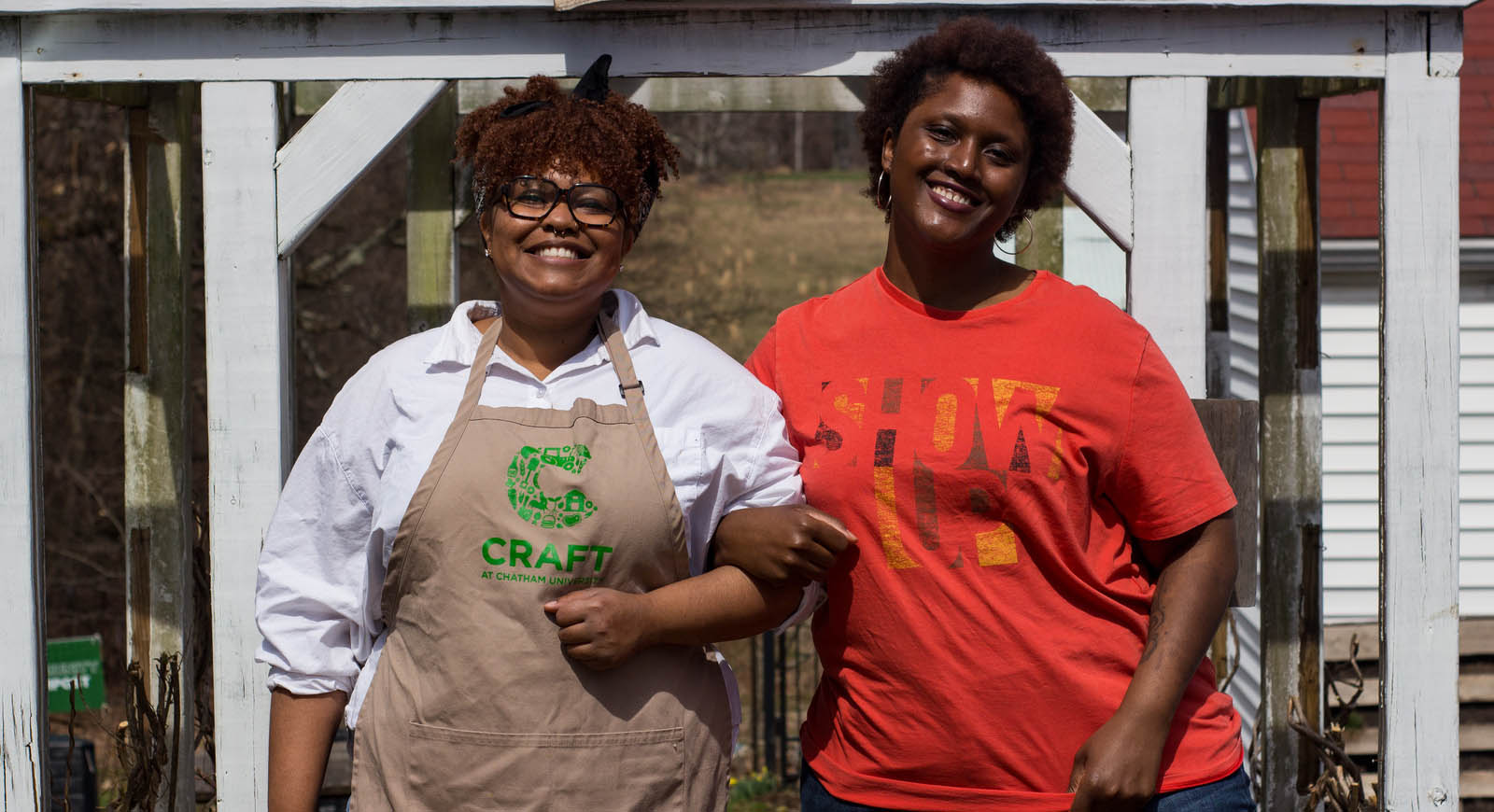 Photo fo two smiling women linking arms. One is wearing an apron with the CRAFT logo.