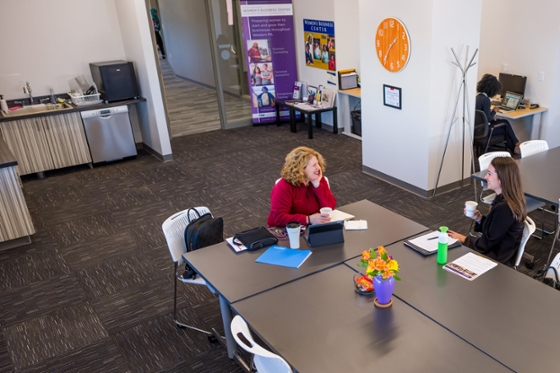 Photo of two women sitting at a conference table at Chatham Eastside, talking and drinking coffee. 