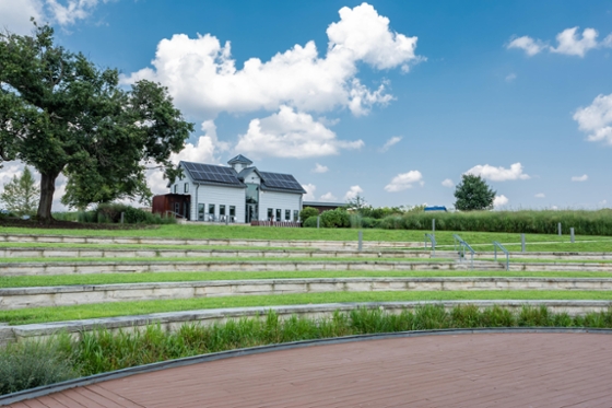 Chatham University's Eden Hall campus amphitheater with rows of built-in shelves sits at the bottom of a hill looking up to a white dairy barn with a solar panel roof. 