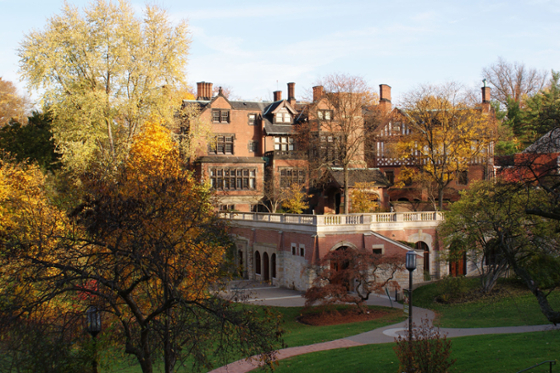 A red-bricked Mellon Hall on Chatham University's Shadyside campus sits on a green campus surrounded by colorful autumn leaves. 