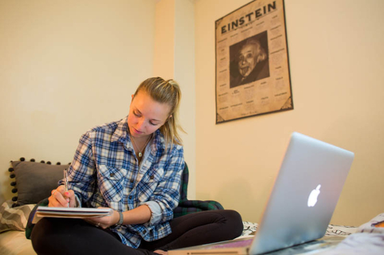 Photo of a student sitting on their dorm room bed and working at a computer