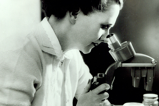 Photo of Rachel Carson, in black and white, looking through a microscope