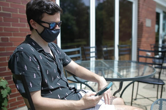 Photo of a Chatham University in a mask, outside, looking at his phone.
