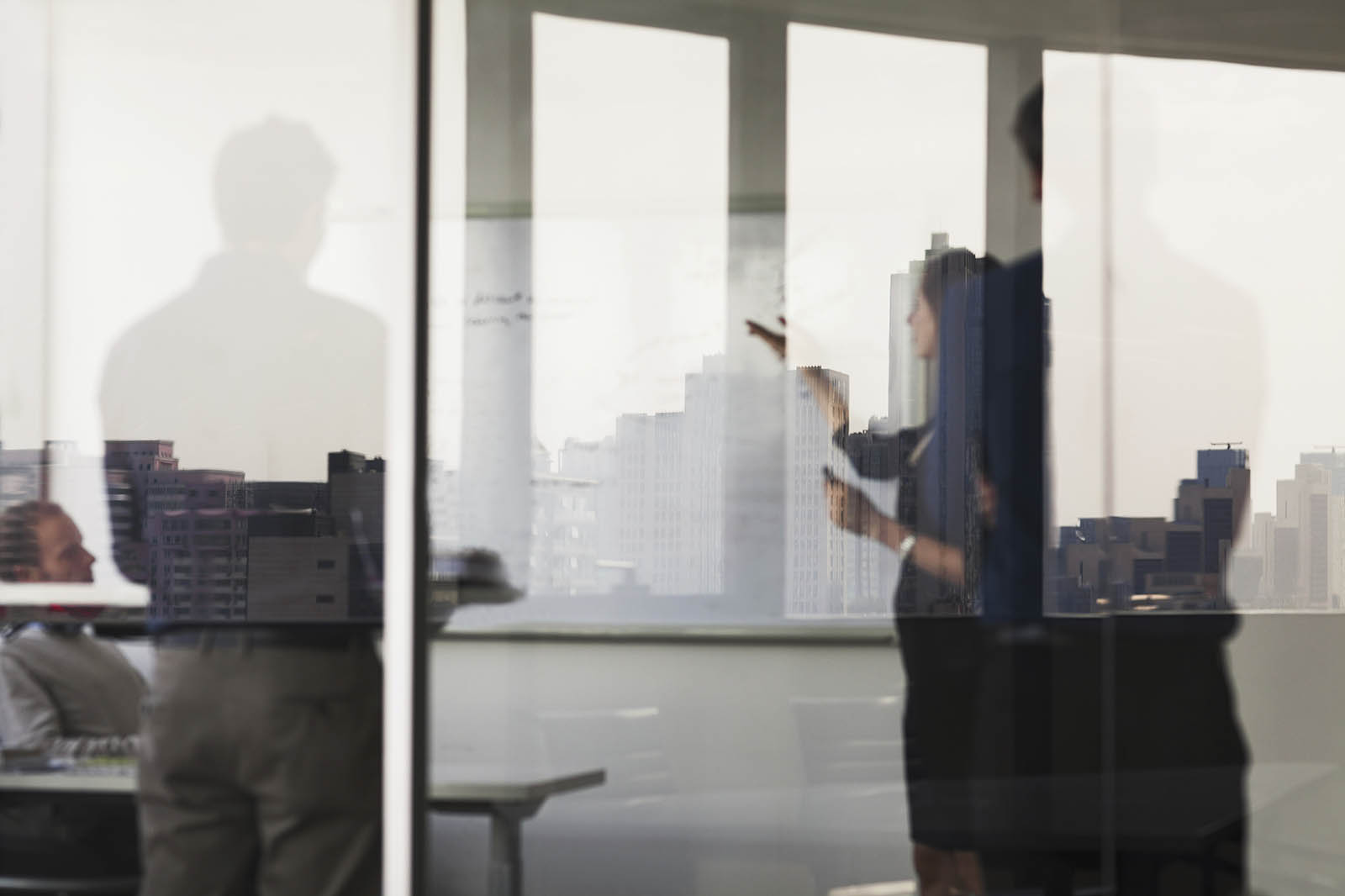 Photo of three people in a professional office building behind glass walls, writing on a board and talking