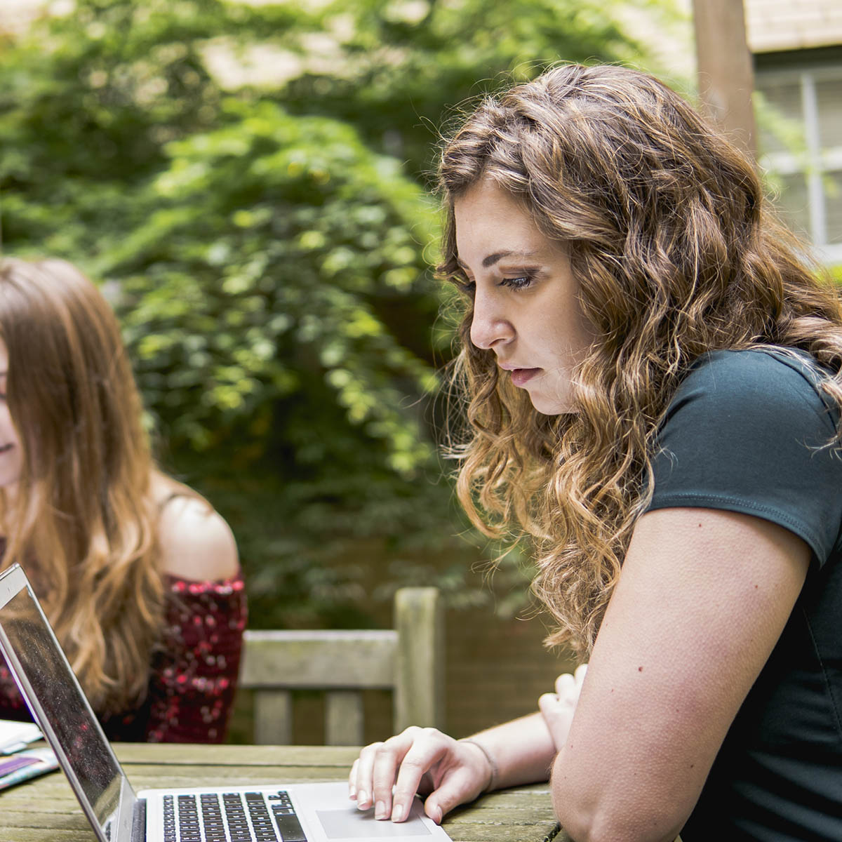 Photo of a student working on her computer at a table outside