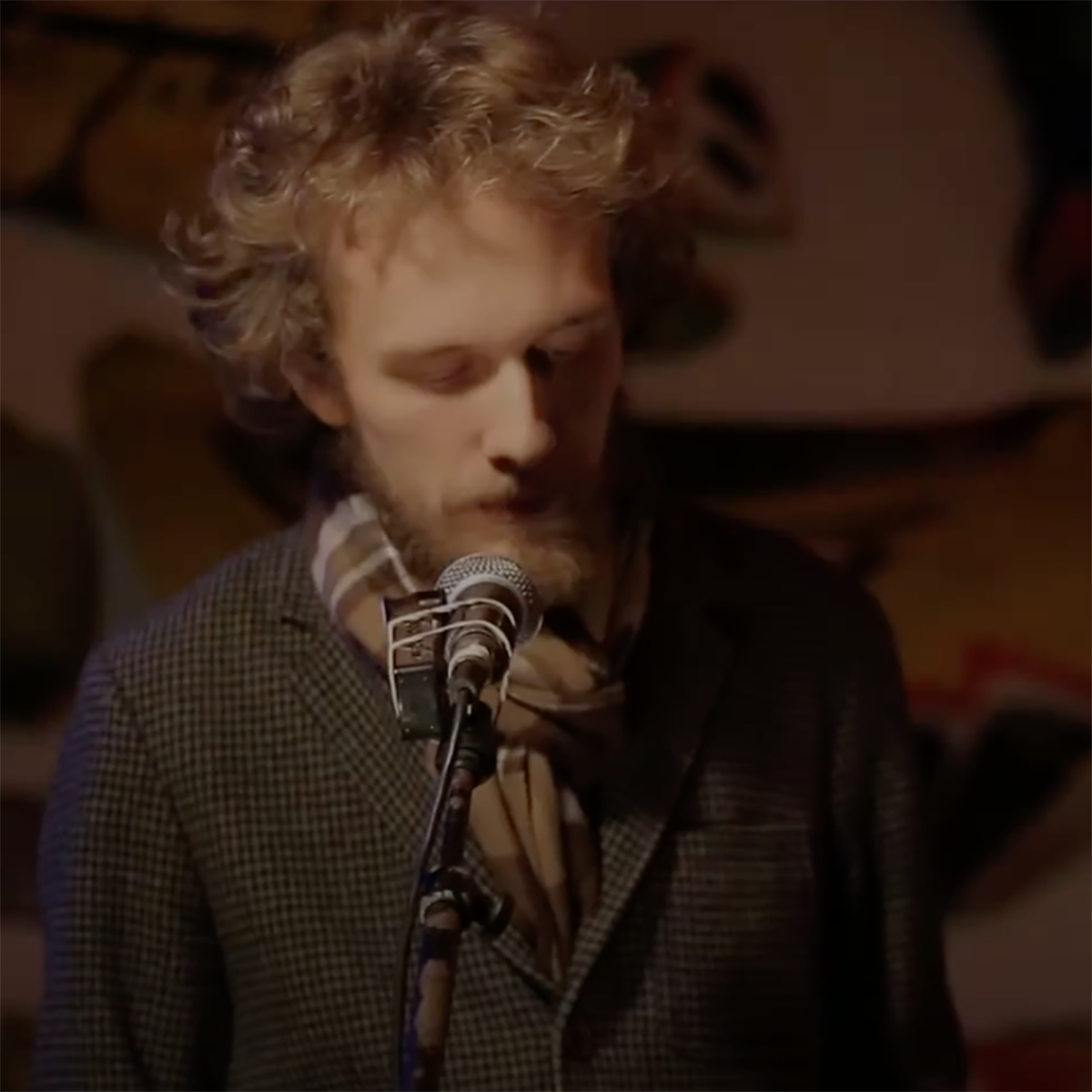 Photo of a man closing his eyes and looking down mid-poetry performance, with a microphone in front of him