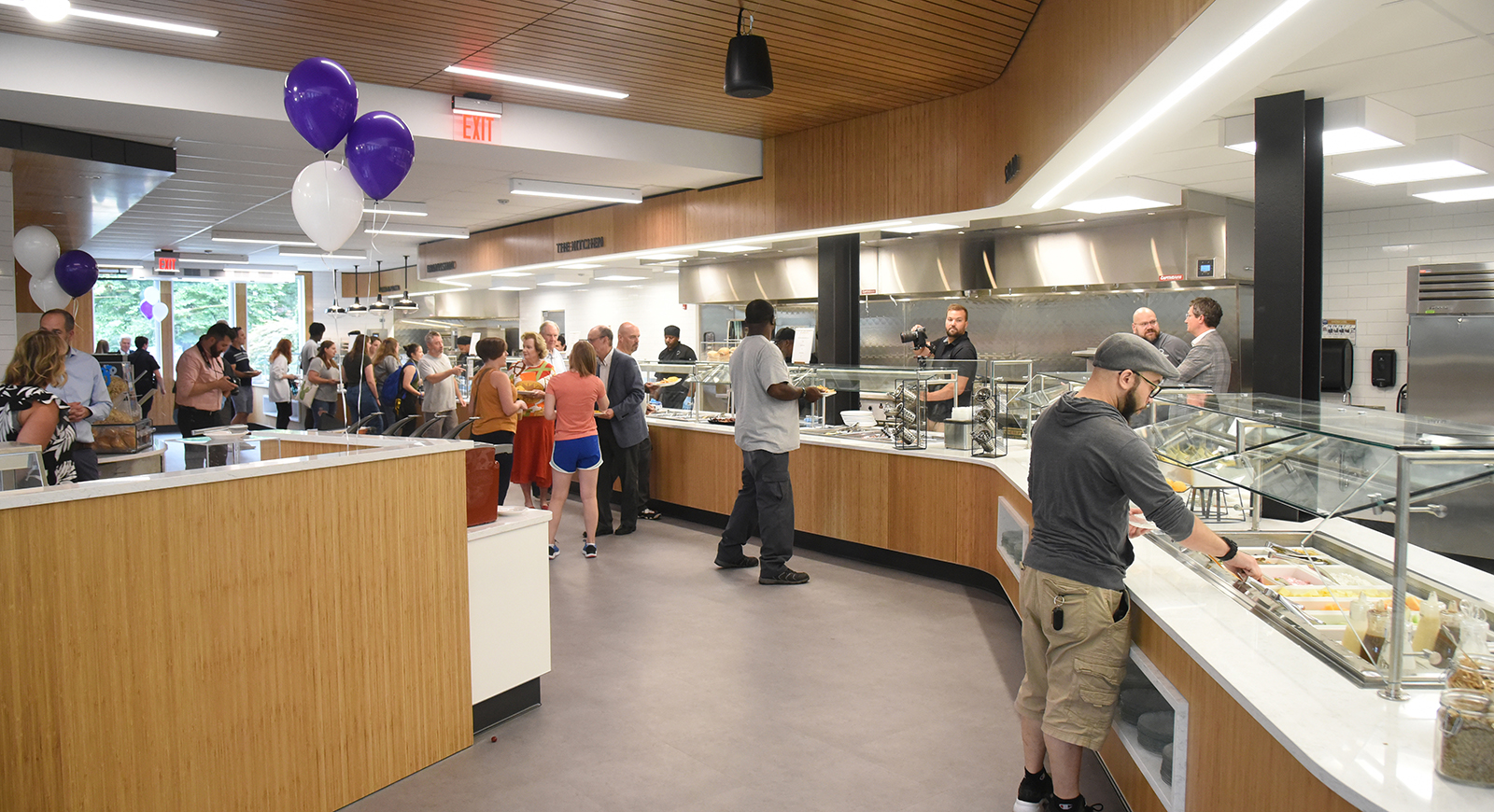 Photo of people serving food to themselves in Anderson Dining Hall on opening day, with some purple balloons nearby