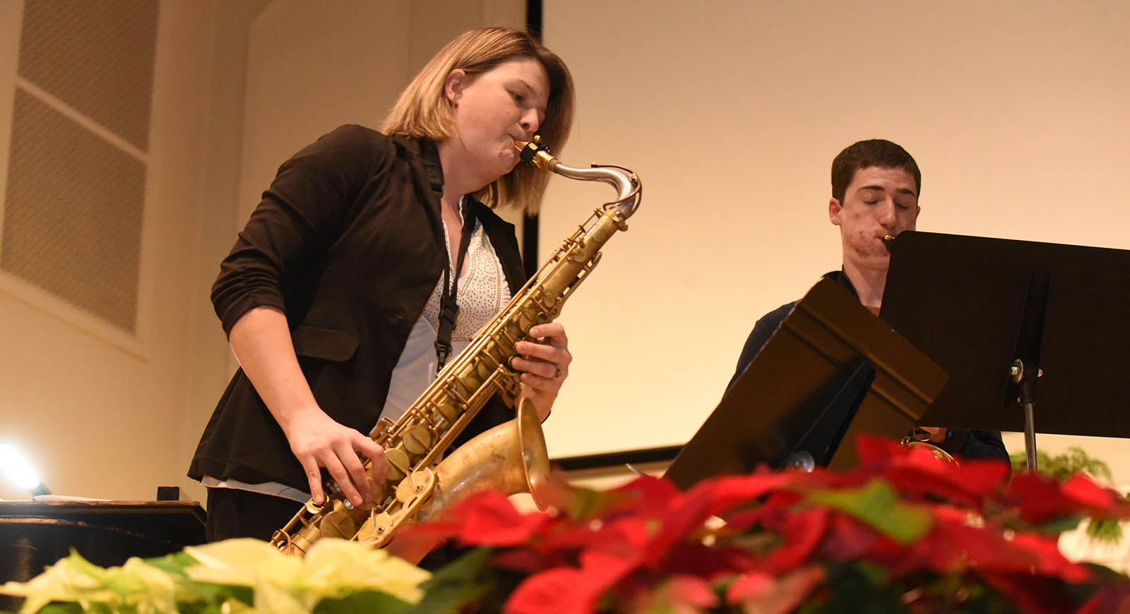 Photo of a woman playing a saxophone with poinsettas in the foreground