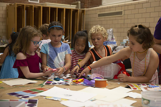 Children gather around a table working on art projects together